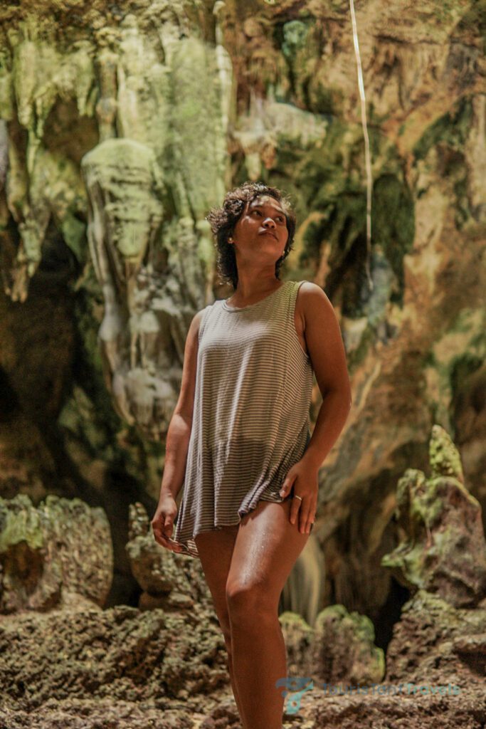 A woman in a striped black and white tank top stands confidently in Bukilat cave, surrounded by rocky terrain.