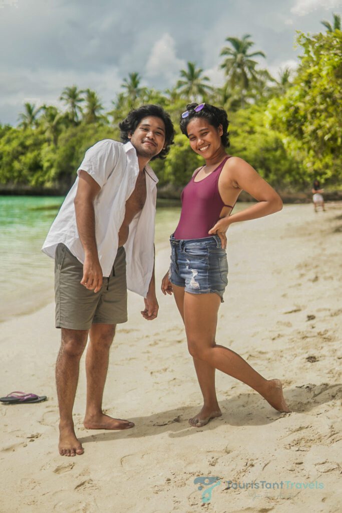 A man and woman standing and smiling barefoot on the white sand beach.