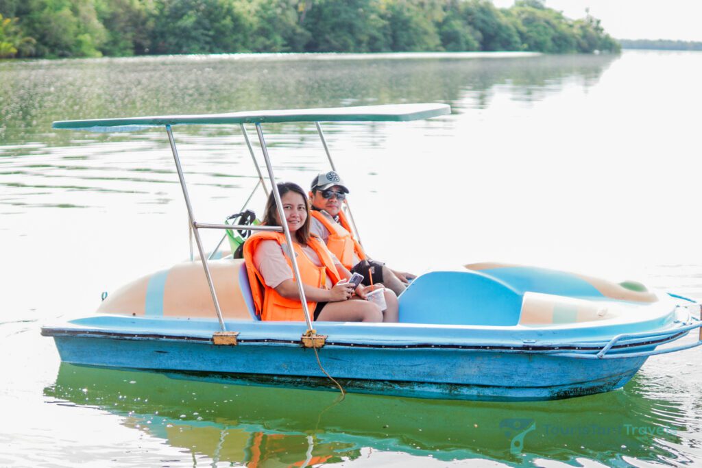 Two people wearing life jackets on a paddle boat on the lake.