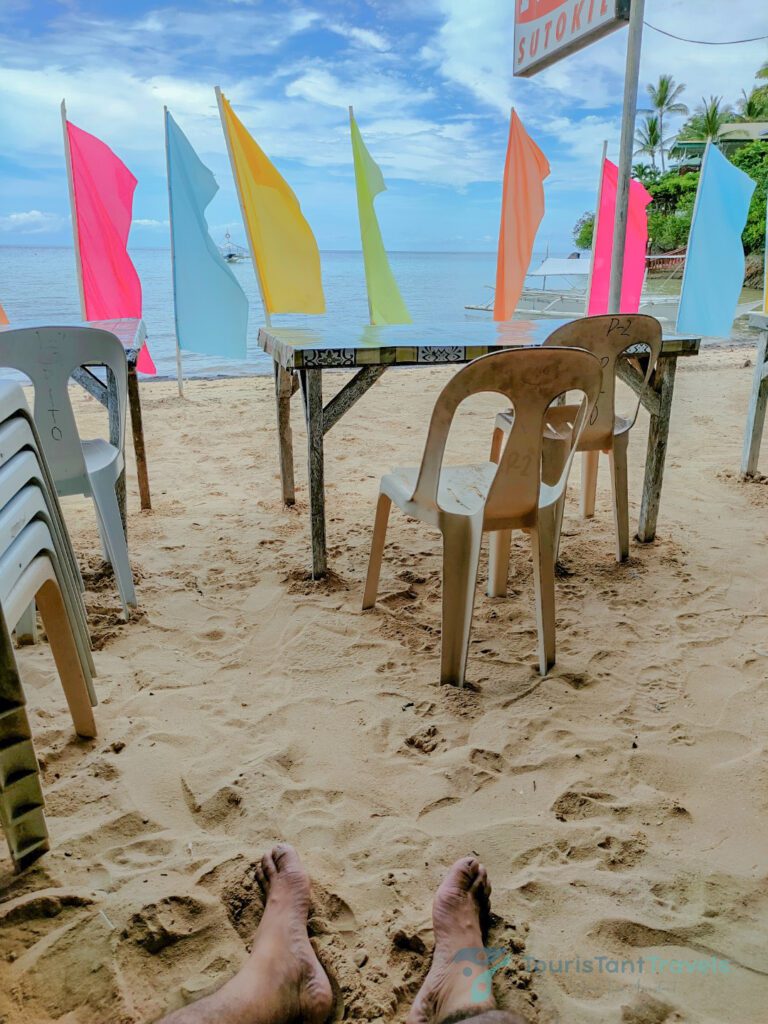 A foot on the sand with chairs and a table on Santiago Bay with colorful flags