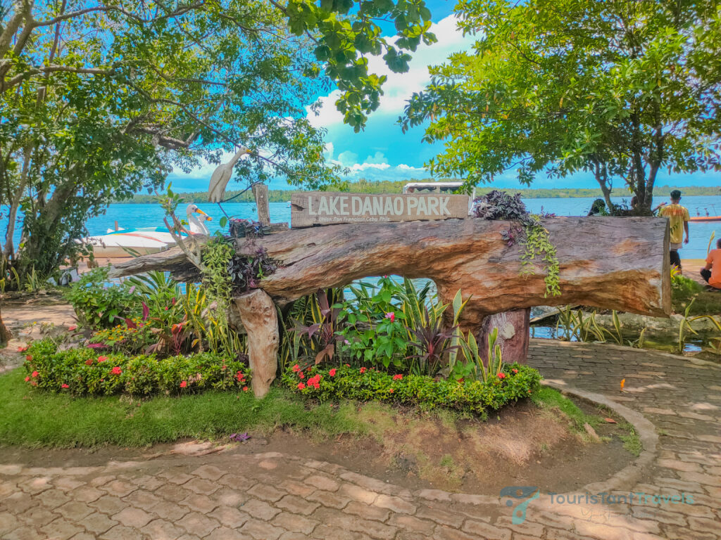 A Lake Danao Park signage with a lush greenery surrounding and a lake background with a people on the right side.
