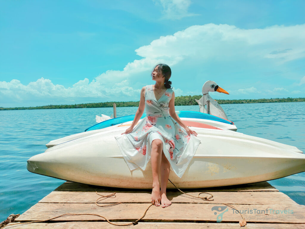 A woman wearing a floral dress posing on a kayak with a lake background.