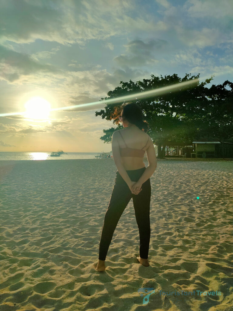 A woman posing and facing the sun during a sunset on a beach.